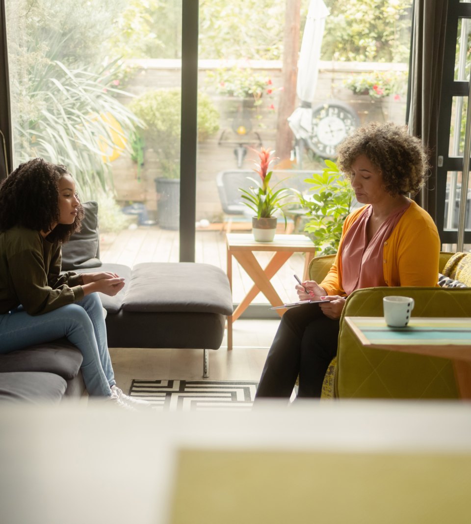 Three women talking in a bright living room full of plants