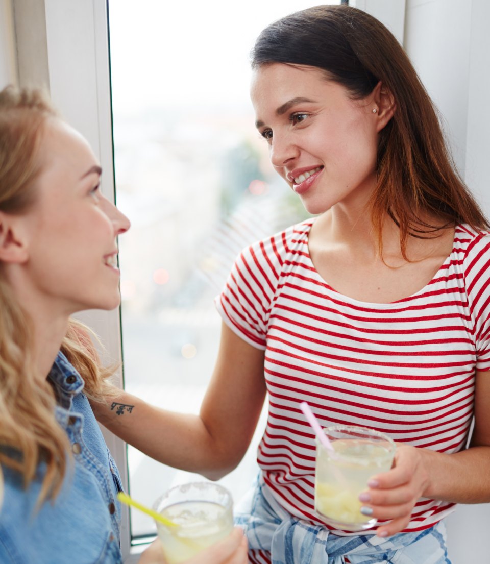 Two young women talking and laughing, one holding a cold drink